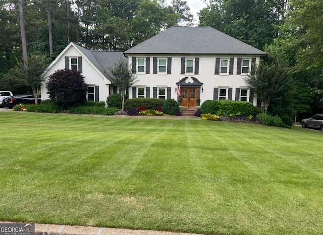 colonial-style house with a front lawn, french doors, and roof with shingles