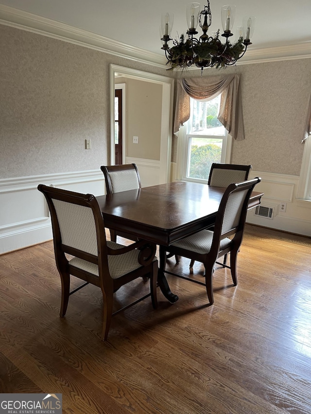dining room featuring crown molding, a chandelier, light wood finished floors, wainscoting, and wallpapered walls