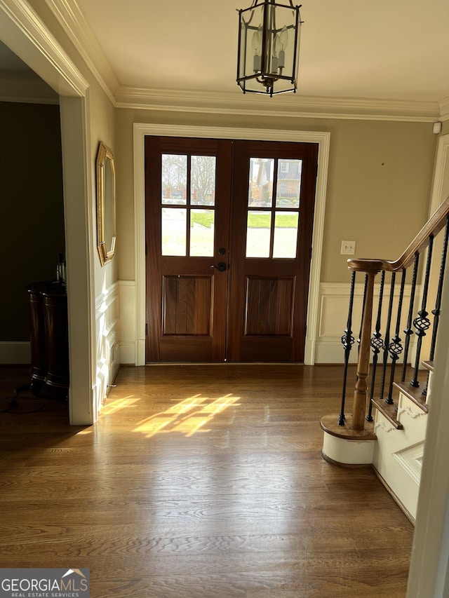 foyer entrance featuring wainscoting, crown molding, wood finished floors, and a decorative wall