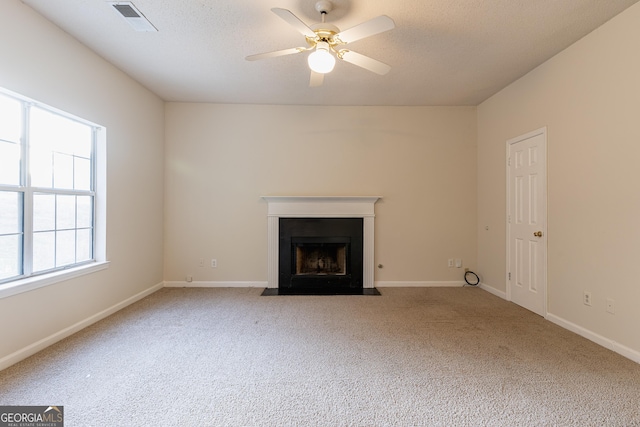unfurnished living room with carpet floors, a fireplace with flush hearth, baseboards, visible vents, and ceiling fan