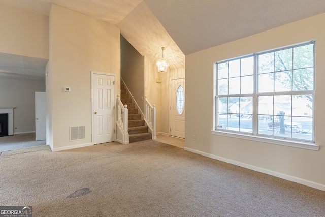 carpeted foyer entrance with visible vents, baseboards, a fireplace, stairway, and an inviting chandelier