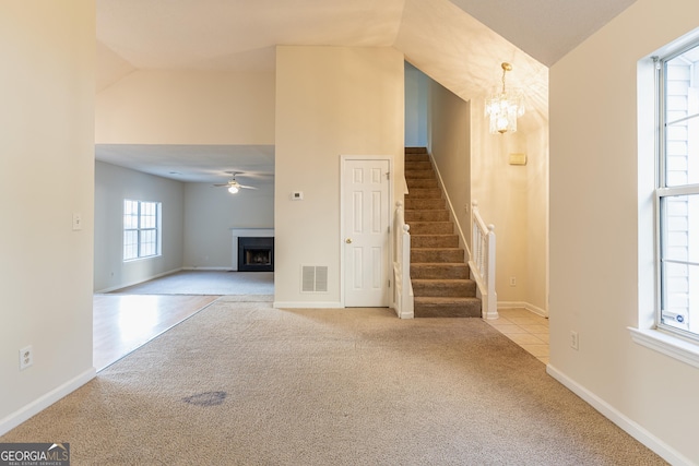 unfurnished living room featuring carpet flooring, visible vents, stairs, a fireplace, and ceiling fan with notable chandelier