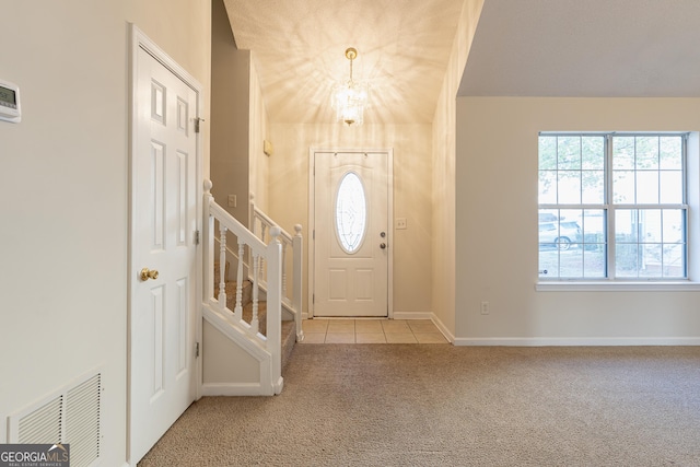 foyer entrance featuring tile patterned flooring, stairway, an inviting chandelier, carpet, and visible vents