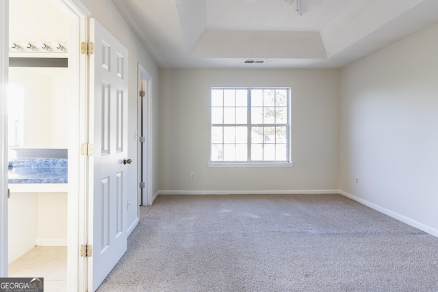 empty room featuring a tray ceiling, baseboards, light colored carpet, and visible vents