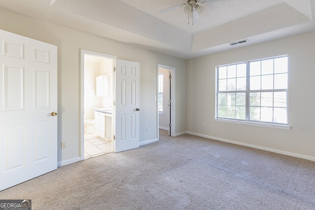 unfurnished bedroom featuring carpet flooring, visible vents, baseboards, ensuite bath, and a tray ceiling