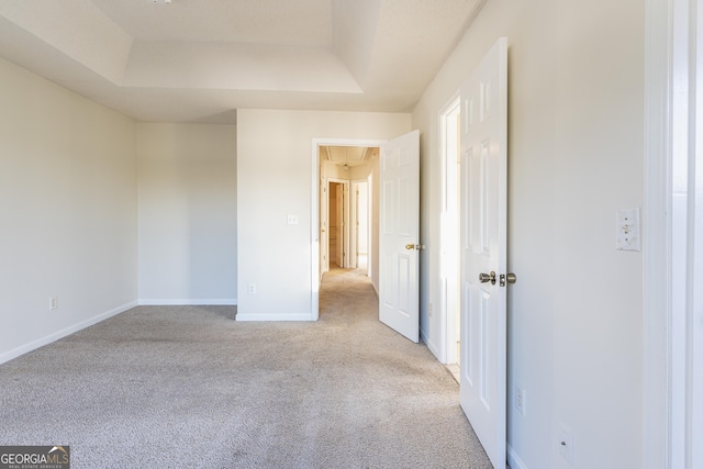 unfurnished bedroom featuring carpet floors, a tray ceiling, and baseboards