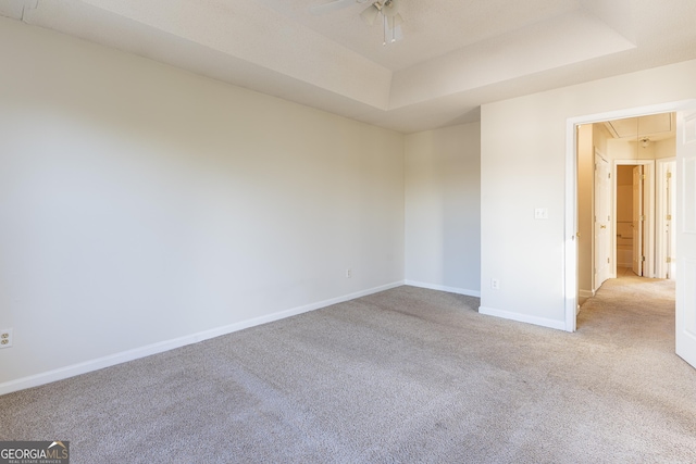 unfurnished room with a tray ceiling, attic access, carpet flooring, baseboards, and ceiling fan