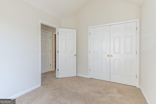 unfurnished bedroom featuring light carpet, baseboards, lofted ceiling, and a closet
