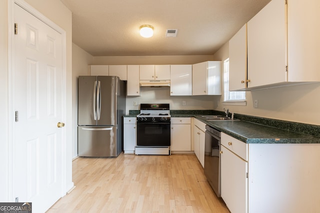 kitchen with gas range, under cabinet range hood, dishwasher, visible vents, and freestanding refrigerator