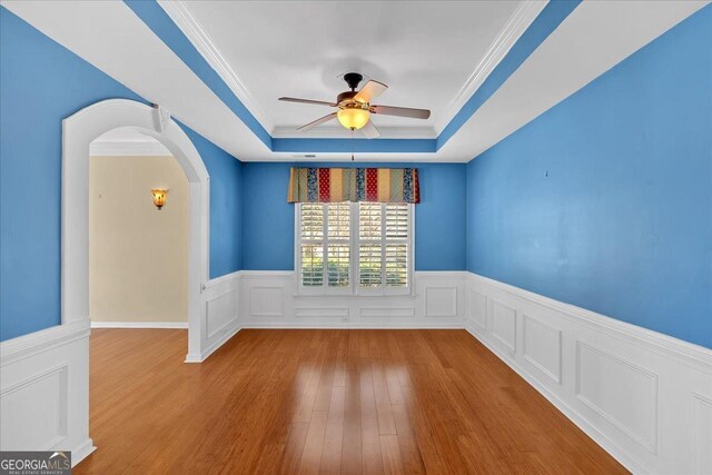 2445 Ridgelake Dr, Villa Rica, GA 30180 - empty room featuring a raised ceiling, a ceiling fan, wood finished floors, a wainscoted wall, and arched walkways
