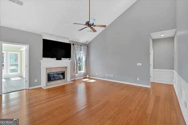 2445 Ridgelake Dr, Villa Rica, GA 30180 - unfurnished living room featuring ceiling fan, light wood-type flooring, a glass covered fireplace, high vaulted ceiling, and a wainscoted wall