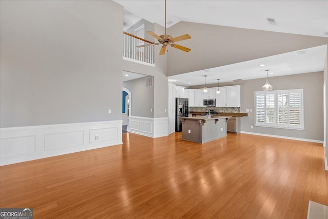 2445 Ridgelake Dr, Villa Rica, GA 30180 - unfurnished living room with ceiling fan, light wood-style flooring, arched walkways, wainscoting, and high vaulted ceiling