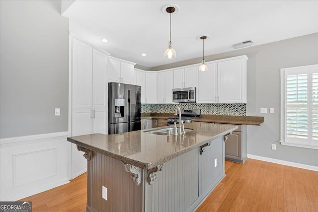 2445 Ridgelake Dr, Villa Rica, GA 30180 - kitchen with stainless steel appliances, light wood finished floors, decorative backsplash, white cabinetry, and a wainscoted wall