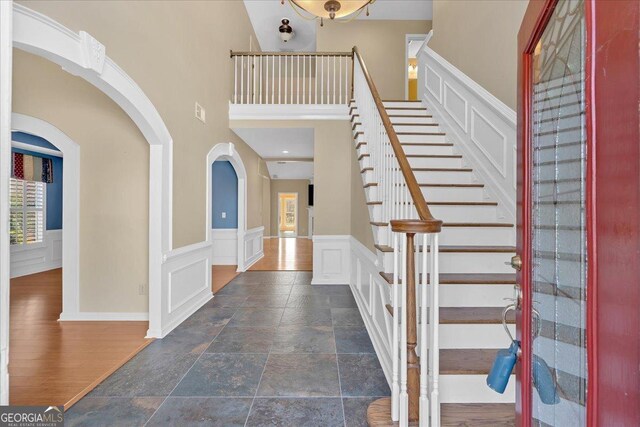 2445 Ridgelake Dr, Villa Rica, GA 30180 - entrance foyer featuring stairway, a decorative wall, a wainscoted wall, stone tile flooring, and a towering ceiling