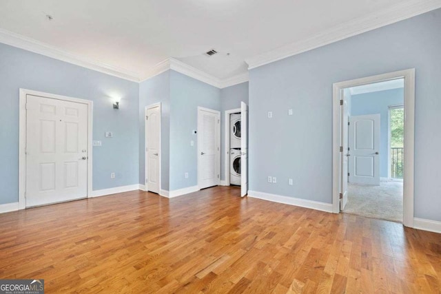 interior space featuring crown molding, baseboards, stacked washer and dryer, light wood finished floors, and visible vents