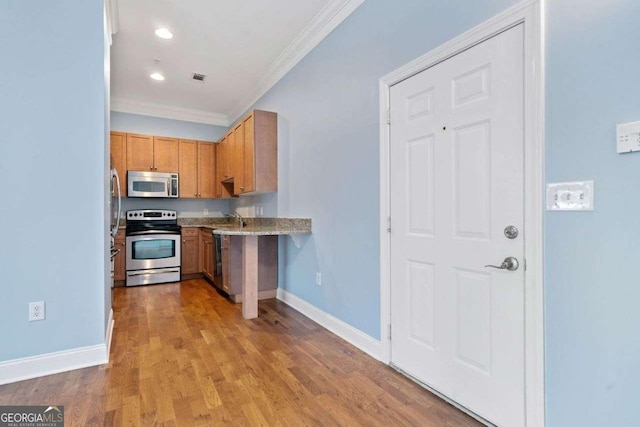 kitchen with a sink, wood finished floors, stainless steel appliances, baseboards, and ornamental molding