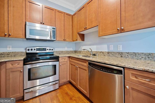 kitchen featuring light wood-style flooring, ornamental molding, appliances with stainless steel finishes, a sink, and light stone counters