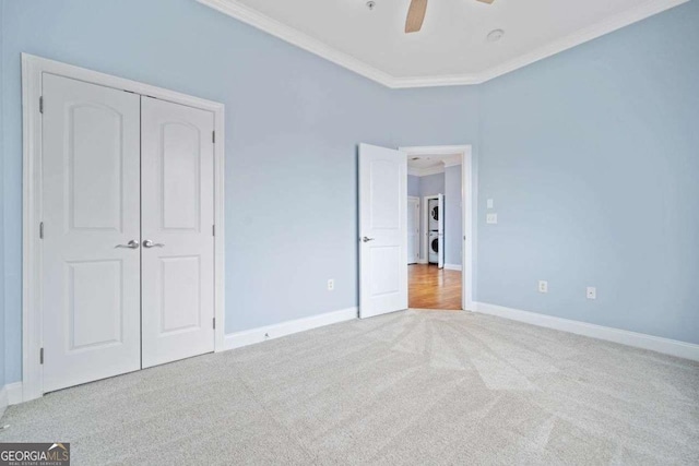 unfurnished bedroom featuring a closet, carpet flooring, baseboards, ornamental molding, and stacked washer / drying machine