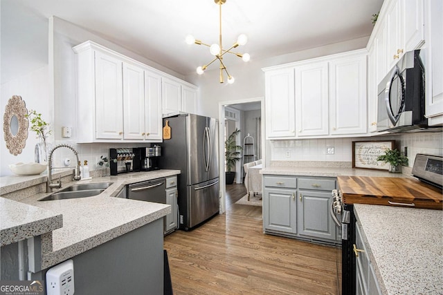 kitchen with decorative backsplash, gray cabinets, white cabinetry, a sink, and stainless steel appliances