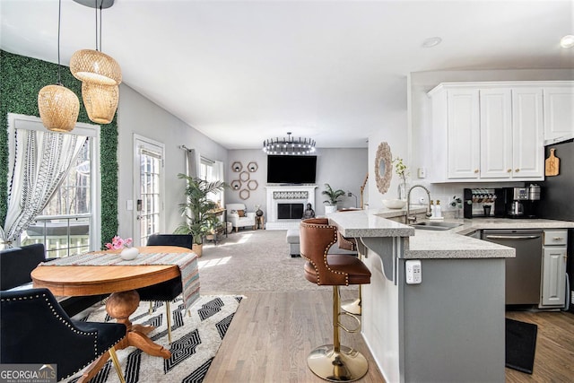 kitchen with a sink, dishwasher, light countertops, a fireplace with raised hearth, and a peninsula