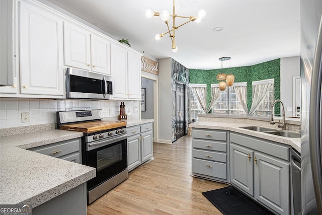 kitchen with white cabinets, a sink, a notable chandelier, gray cabinetry, and stainless steel appliances