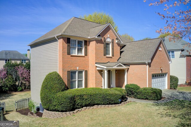 traditional-style home with fence, an attached garage, a front lawn, brick siding, and a shingled roof