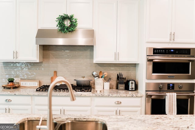 5745 Pickens Garden Ln, Powder Springs, GA 30127 - kitchen featuring stainless steel appliances, extractor fan, white cabinetry, decorative backsplash, and light stone counters