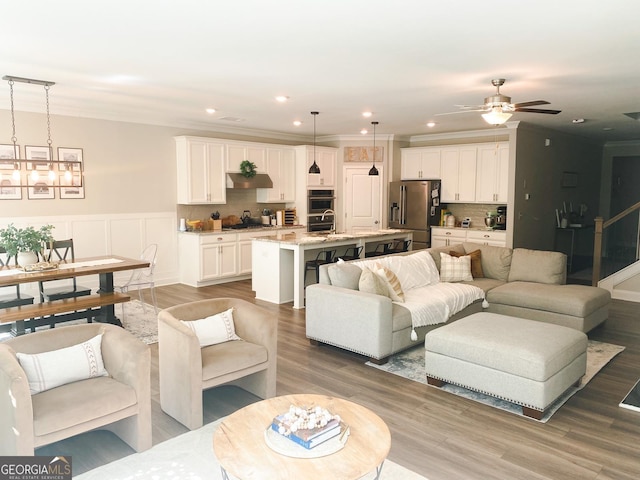 5745 Pickens Garden Ln, Powder Springs, GA 30127 - living room featuring light wood finished floors, a ceiling fan, recessed lighting, wainscoting, and crown molding