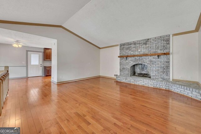 2285 Bascomb Carmel Rd, Woodstock, GA 30189 - unfurnished living room featuring vaulted ceiling, a textured ceiling, a brick fireplace, light wood-style flooring, and crown molding