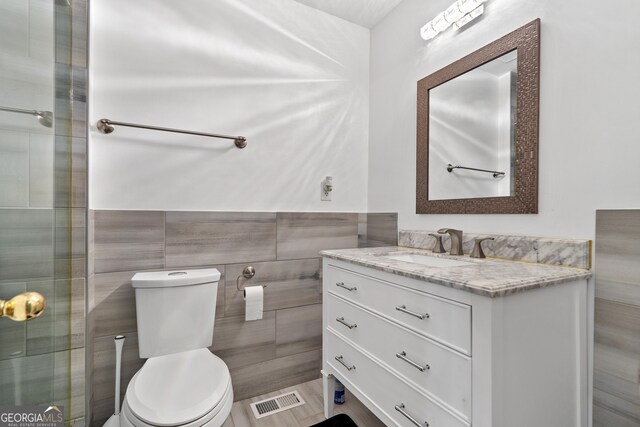 bathroom with a shower stall, toilet, and a wainscoted wall