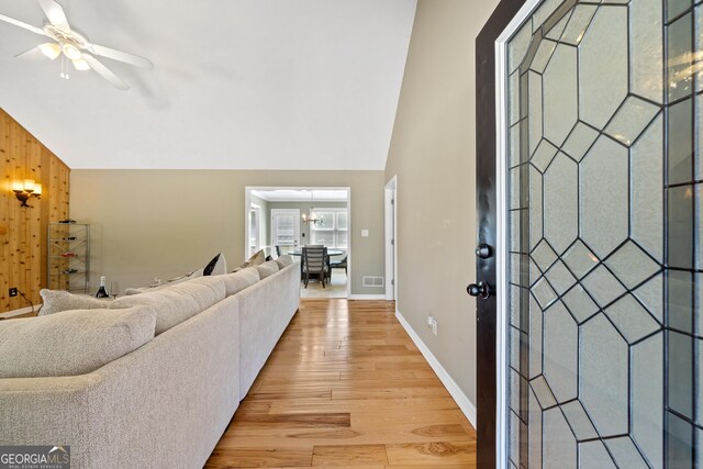 living room featuring high vaulted ceiling, wood finished floors, baseboards, and wood walls