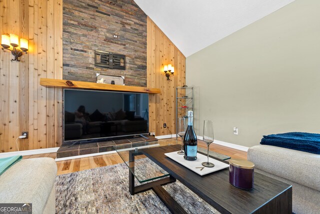 living area with wood walls, wood finished floors, a ceiling fan, high vaulted ceiling, and baseboards