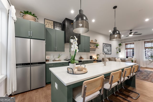 kitchen with green cabinetry, light countertops, light wood-type flooring, freestanding refrigerator, and a ceiling fan