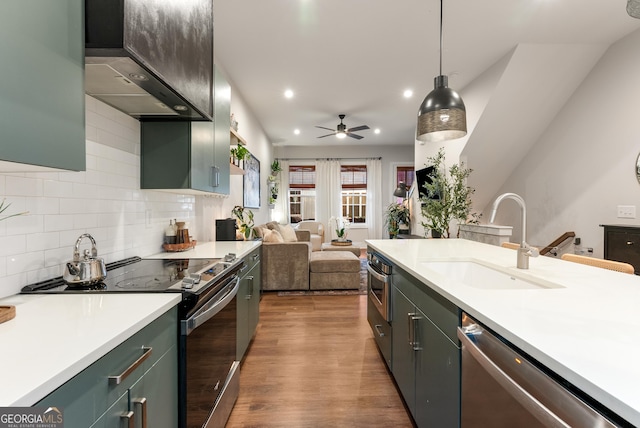 kitchen featuring a sink, wall chimney range hood, light countertops, appliances with stainless steel finishes, and wood finished floors