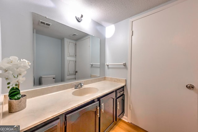 bathroom featuring toilet, vanity, wood finished floors, a textured ceiling, and visible vents
