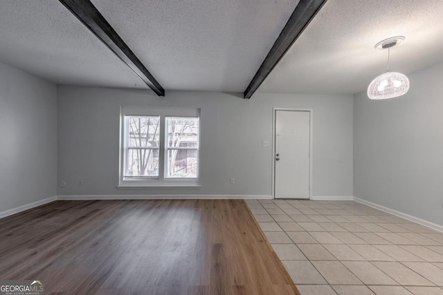 empty room with baseboards, a textured ceiling, light wood-type flooring, and beamed ceiling