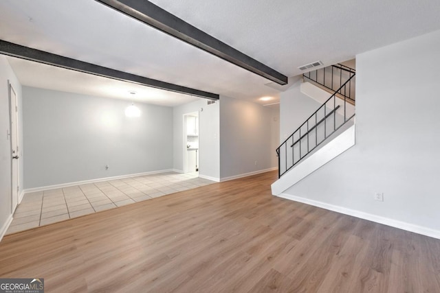 unfurnished living room featuring beamed ceiling, visible vents, wood finished floors, and stairs