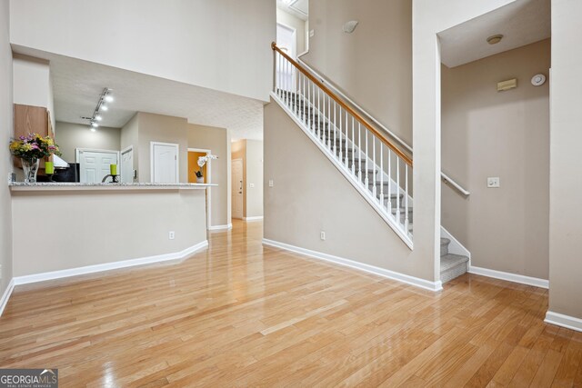 810 Abbotts Mill Ct Unit 83, Duluth, GA 30097 - unfurnished living room with baseboards, rail lighting, stairway, a high ceiling, and wood-type flooring