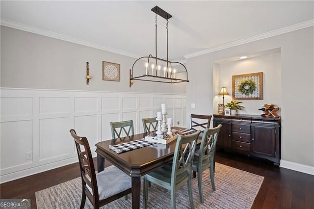 dining space featuring a wainscoted wall, a decorative wall, crown molding, dark wood-type flooring, and a notable chandelier