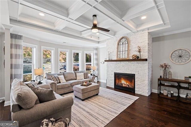 living area with coffered ceiling, ornamental molding, hardwood / wood-style flooring, ceiling fan, and a stone fireplace