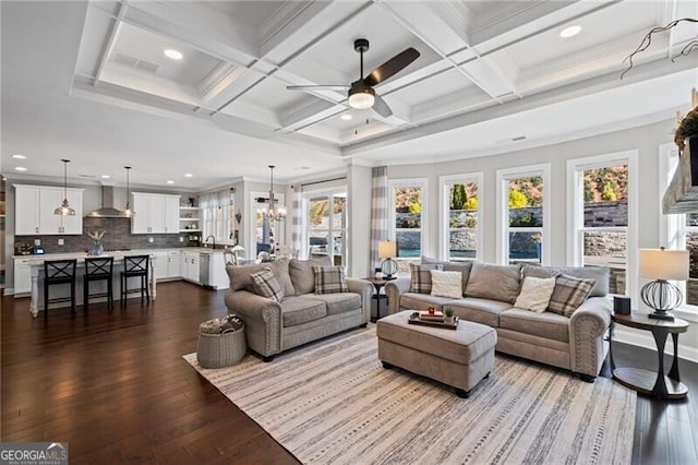 living area featuring dark wood-style flooring, ceiling fan with notable chandelier, beamed ceiling, and coffered ceiling