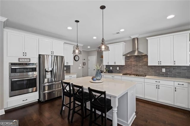 kitchen with light countertops, crown molding, stainless steel appliances, wall chimney range hood, and white cabinets