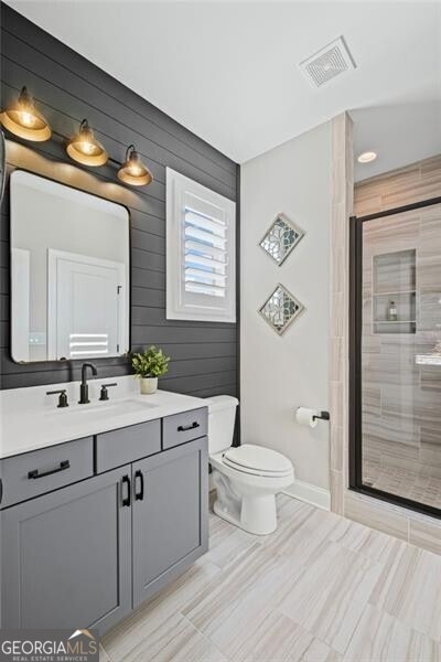full bath with visible vents, baseboards, toilet, vanity, and a stall shower