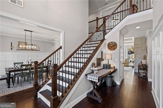 stairs featuring ornamental molding, a chandelier, a towering ceiling, hardwood / wood-style flooring, and visible vents