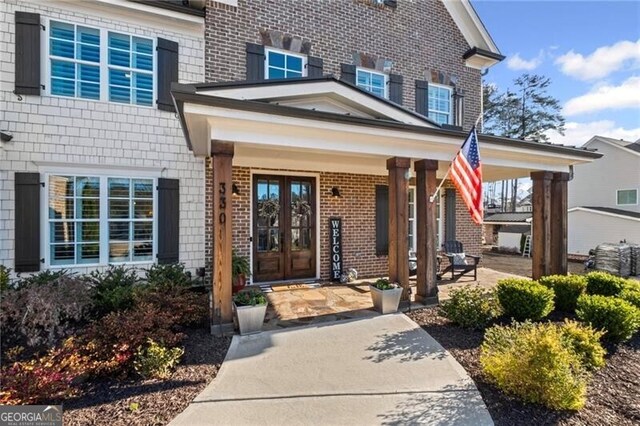 property entrance featuring french doors, brick siding, and a porch