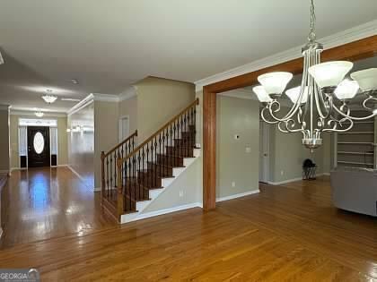 foyer entrance with baseboards, stairs, ornamental molding, wood finished floors, and a notable chandelier