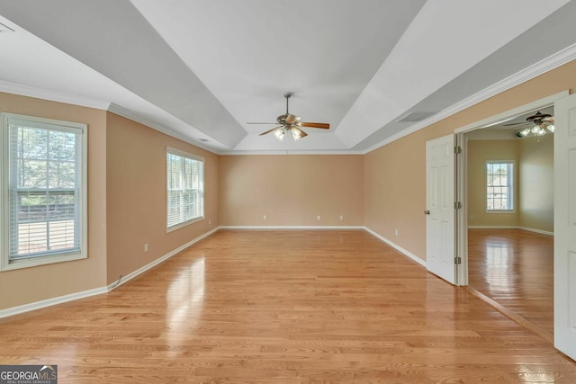 empty room featuring plenty of natural light, a ceiling fan, and a raised ceiling