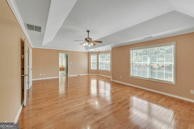 unfurnished room with light wood-type flooring, ornamental molding, a raised ceiling, visible vents, and a ceiling fan