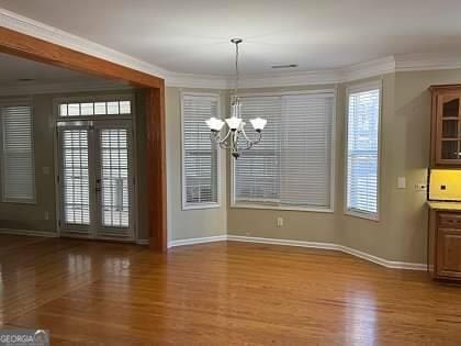 unfurnished dining area with a notable chandelier, wood finished floors, and ornamental molding