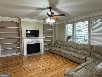 unfurnished living room featuring ceiling fan, crown molding, wood finished floors, and built in features
